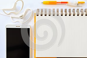 Yellow pen on a notebook and cell phone with earphone on white b