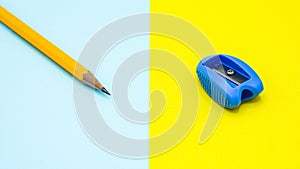 Yellow pencil and a blue plastic pencil sharpener on blue and yellow desk.