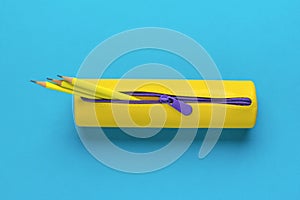 Yellow pencil case with three yellow pencils on a blue background. Flat lay
