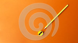 Yellow pencil and sharpener on an orange background.
