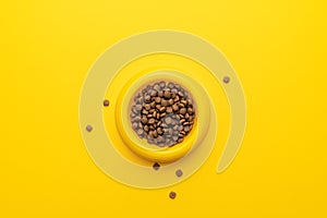 Yellow pet bowl full of dry food over yellow background with copy space