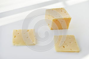 Yellow pieces of cheese on a white background. Square cheese. Delicious cheese snack