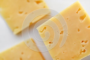 Yellow pieces of cheese on a white background. Square cheese. Delicious cheese snack