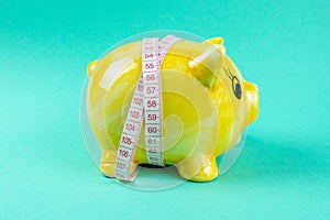 Yellow piggy bank in the form of a pig wrapped with measuring tape on a light green background. The concept of saving money for