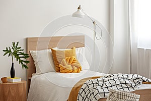 Yellow pillows and cozy blanket on single bed in elegant hotel room,green leaf in black vase on wooden bedside table