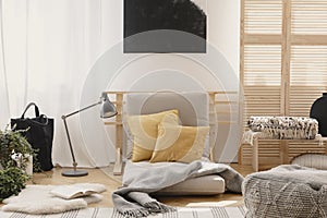Yellow pillows and grey warm blanket on grey futon in bright natural bedroom interior photo