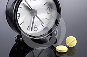 Yellow pills next to a clock