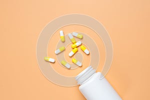 Yellow pills, tablets and white bottle on orange background