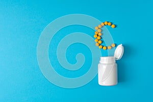 Yellow pills in a vitamin C poured from a medicine bottle on blue background. Medication and prescription pills. Top view. Flat la