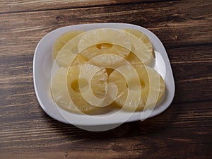 Yellow pineapple rings on a white plate on a wooden table close up.