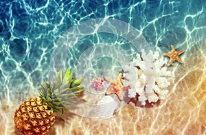 Yellow pineapple, seashells and starfish on a blue water background.