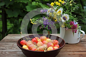 Yellow and pink cherries in a bowl, and midsummer wild flowers on a vintage wooden board background.