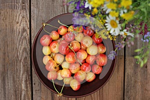 Yellow and pink cherries in a bowl, and midsummer wild flowers on a vintage wooden board background.