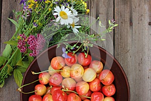 Yellow and pink cherries in a bowl, and midsummer wild flowers on a vintage wooden board background.