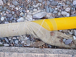 Yellow pipe on stone pebbles. Technical communications on the beach. Cable