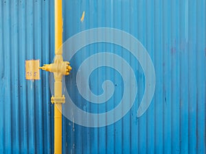Yellow pipe with valve on the blue wall background