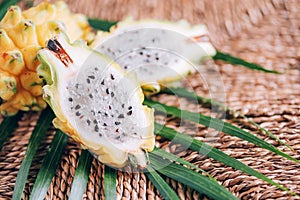 Yellow pitahaya pitaya or dragon fruit with palm leaves on rattan background. Copy space. Creative design banner. Summer time.