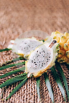 Yellow pitahaya pitaya or dragon fruit with palm leaves on rattan background. Copy space. Creative design banner. Summer time.