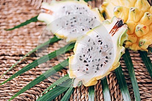 Yellow pitahaya pitaya or dragon fruit with palm leaves on rattan background. Copy space. Creative design banner. Summer time.