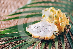 Yellow pitahaya pitaya or dragon fruit with palm leaves on rattan background. Copy space. Creative design banner. Summer time.