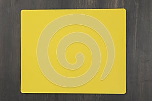 yellow plactic cutting board on dark wood table. Top view, flat lay