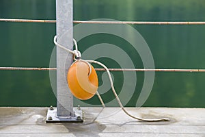 Yellow plastic buoy attached to a metal fence on the bank of a lake with green water