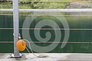Yellow plastic buoy attached to a metal fence on the bank of a lake with green water