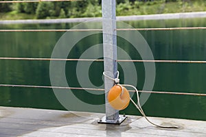 Yellow plastic buoy attached to a metal fence on the bank of a lake with green water