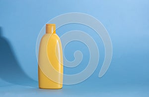 Yellow plastic cosmetic bottle on blue background. Kids hair shampoo, body lotion or sunscreen cream. Mock up, template.