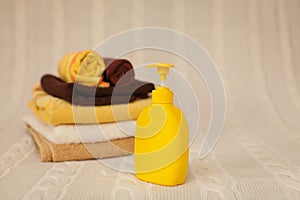 Yellow plastic dispenser with liquid soap and a stack of brown towels on a beige rug in selective focus