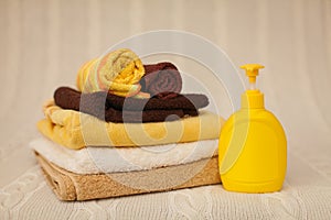 Yellow plastic dispenser with liquid soap and a stack of brown towels on a beige rug in selective focus