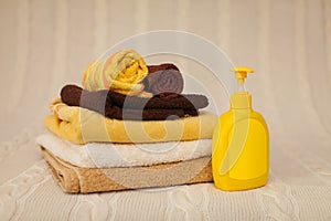 Yellow plastic dispenser with liquid soap and a stack of brown towels on a beige rug in selective focus