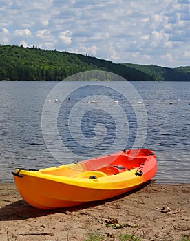 Yellow plastic kayak on sand beach of calm lake hills covered by green trees