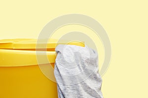 Yellow plastic laundry basket with gray clothing on yellow background