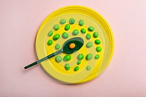 A yellow plastic plate filled with candy with a green spoon on a pink background