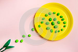 Yellow plastic plate with a path of sweets with green spoons on a pink background