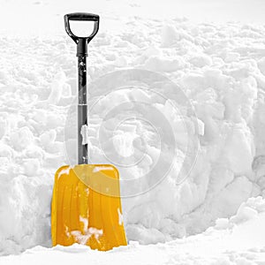 Yellow plastic shovel stuck in fluffy white snow in winter