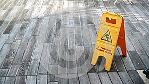Yellow plastic sign with Italian writing Caution wet floor, on geometric stone floor