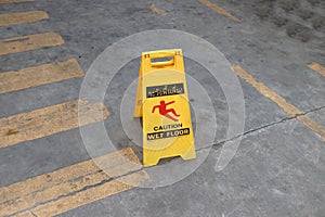 Yellow plastic sign with red symbol of slip and black text of caution wet floor on the floor.