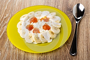 Yellow plate with defatted cottage cheese, slices of banana, jam and yogurt, spoon on table