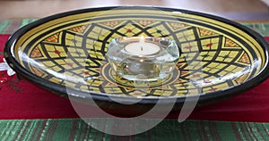 Yellow plate with a glass candle holder, adult female hands lighting a tea light with a match