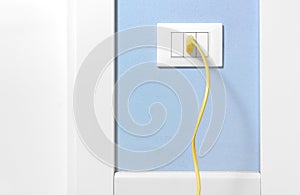 Yellow Plug in a Wall Socket on a Blue Wall
