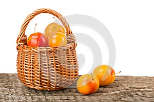 Yellow plums with leaf in a wicker basket on wooden table with white background