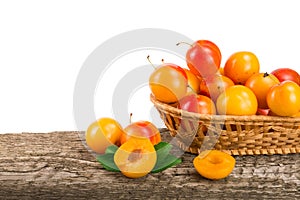 Yellow plums with leaf in a wicker basket on wooden table with white background