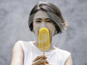 Yellow popsicle in happy smiling beautiful Asian woman`s hand.