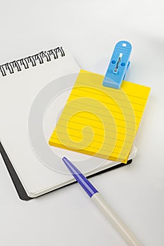 Yellow post note, empty white note, pen and blue clip