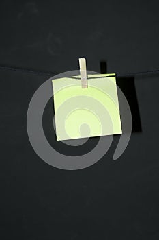 Yellow post it note with wooden clothespin hanging on rope thread with dark background copy space vertical annotation