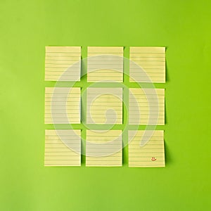 Yellow post-it notes arranged in square of nine , with one note with red smile wright on it. Blue background. minimal creative