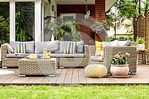 Yellow pouf and flowers next to rattan garden furniture on wooden terrace of house. Real photo