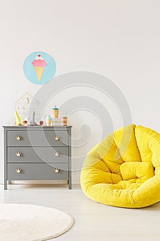 Yellow pouf next to a grey chest of drawers and ice-cream poster